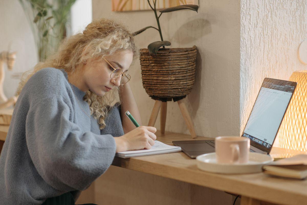 Mujer tomando notas junto a su portátil, preparándose para una sesión de terapia online